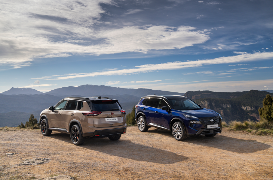 Two Nissan SUVs parked on a hilltop with a mountainous landscape in the background.
