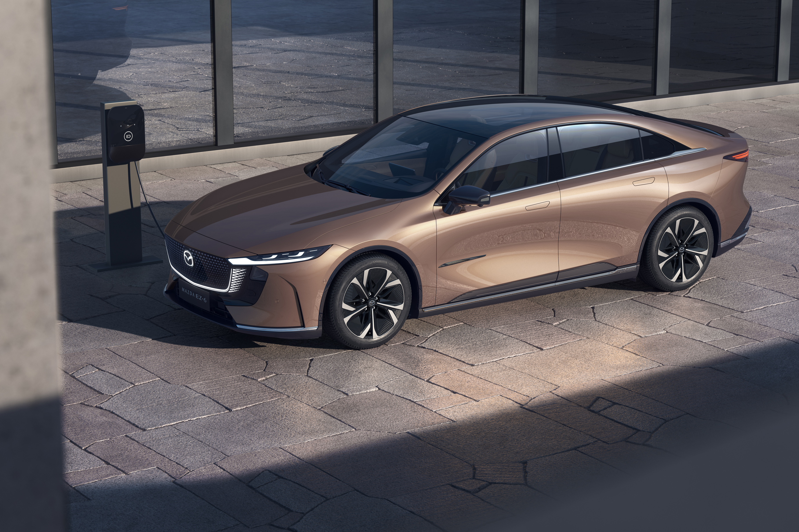 Bronze electric car charging at a station, viewed from the side.
