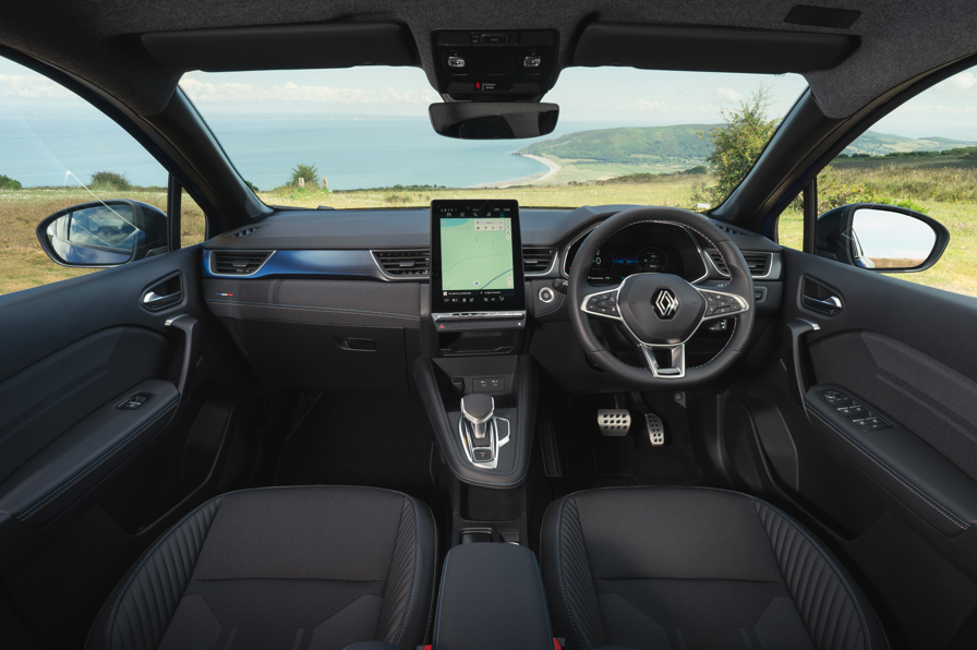 Car interior with digital dashboard and steering wheel, view of coast through the windscreen.