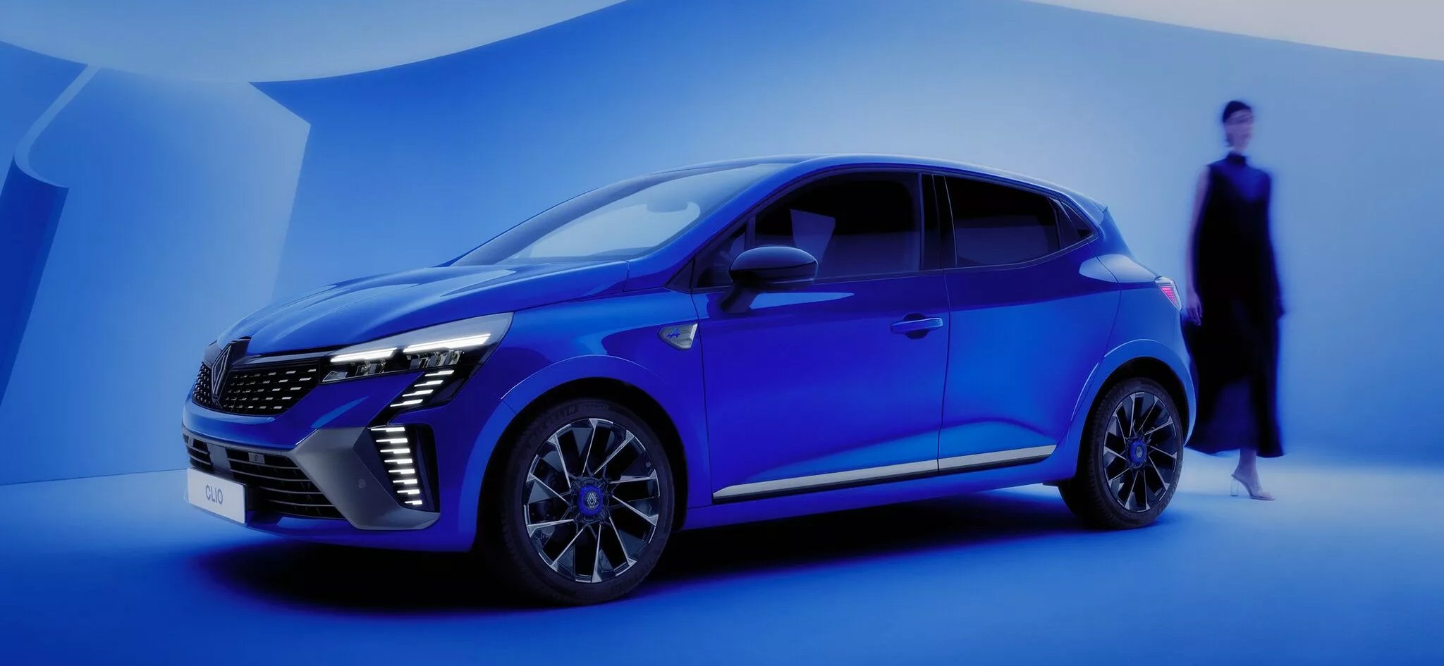 A blue car with a blurred person walking beside it.