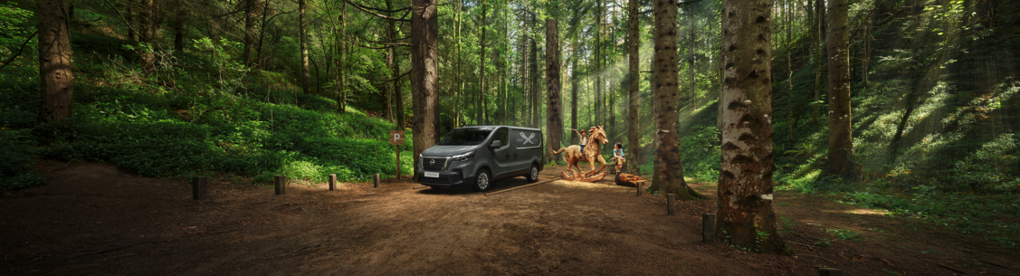 Van parked in a forest near a wooden sculpture with a person standing beside.