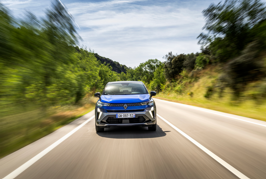 Blue car driving on a road with blurred trees on either side.
