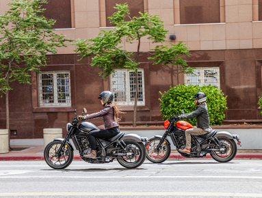 Two motorcyclists riding on an urban street, both wearing helmets and jackets.